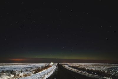 Empty road amidst landscape against star field during winter