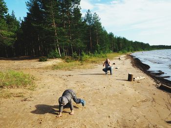 Mature man crouching while photographing grandson playing on shore at beach