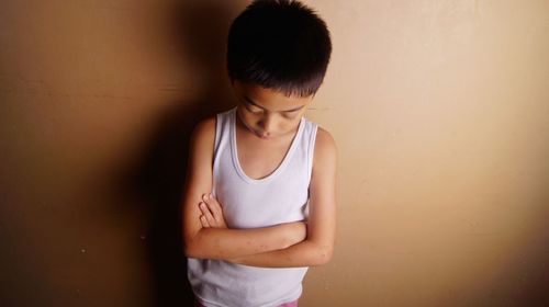 Boy with arms crossed standing against wall at home