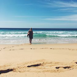 Rear view of man standing on beach against sky