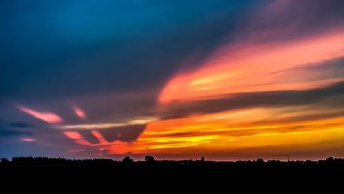 Scenic view of dramatic sky over silhouette landscape during sunset