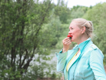 Blond woman eats strawberries in the forest.