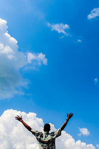 Low angle view of man with arms raised against blue sky