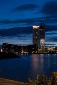 Illuminated buildings by sea against sky at night
