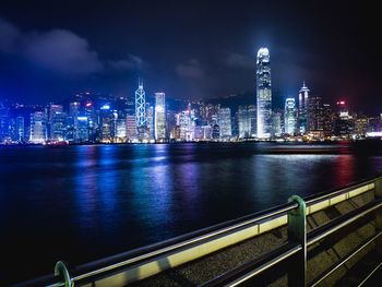 Illuminated city by river against sky at night