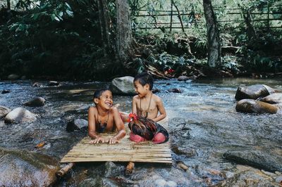 Boys with rooster on wood in stream