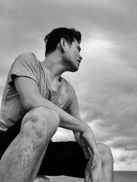 Side view of young man looking away against sky