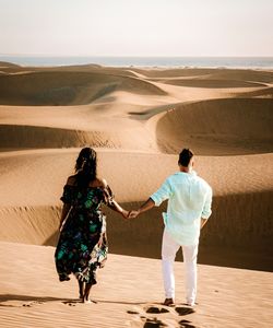 Rear view of people walking on sand dune