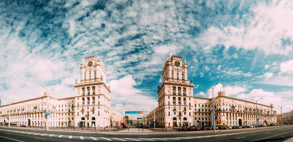 Buildings by road against cloudy sky