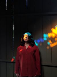 Young woman looking away while standing against illuminated wall