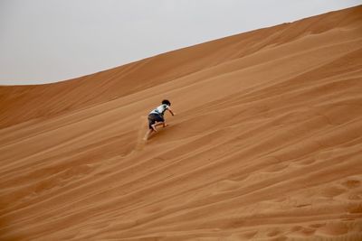 Low angle view of boy climbing on sand dunes at desert