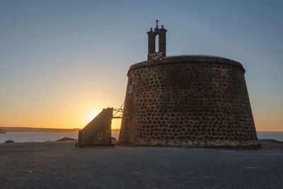 Lighthouse by sea against clear sky during sunset