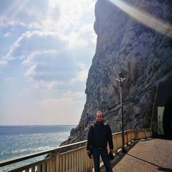 Man standing on railing by sea against sky