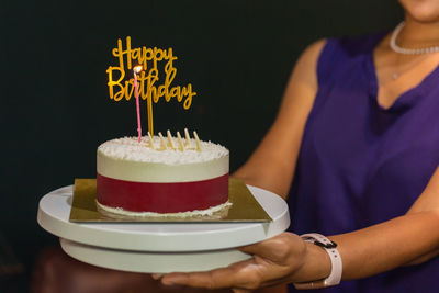 Woman holding birthday cake with candle and birthday plate.