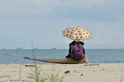 Woman with pink umbrella on beach against sky