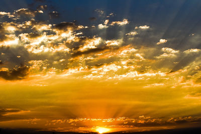 Low angle view of sunlight streaming through clouds during sunset