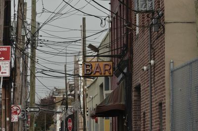 Low angle view of bar sign on building with tangled electricity cables