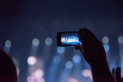 Cropped hand of man photographing during music concert at night