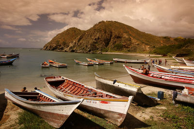 Fishing boats moored at beach by mountains against sky
