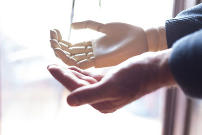 Cropped image of man holding robot hand against window