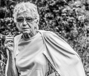 Portrait of senior woman smoking while standing against plant