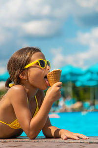 Cute girl eating ice cream by swimming pool