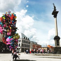 Woman with cartoon shape balloons at town square against sky