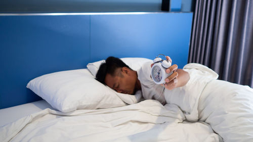 Man with alarm clock sleeping on bed at home
