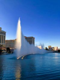 Fountain in city against clear blue sky