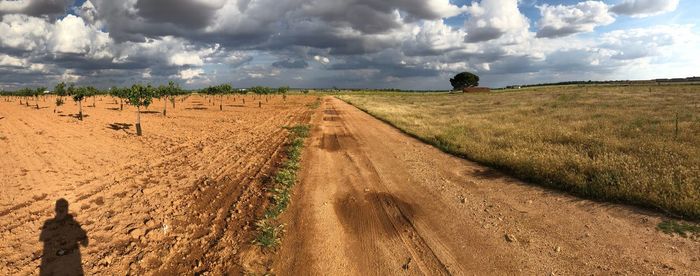 Panoramic view of dirt road on field against sky