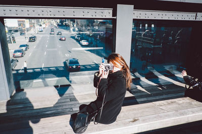 Woman photographing with camera while sitting on bench