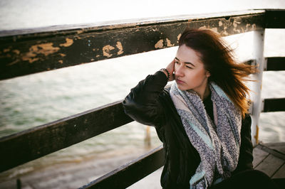 Thoughtful young woman sitting on pier over sea