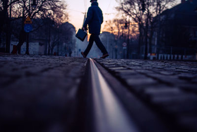 Full length of man crossing railroad track on street in city during sunset