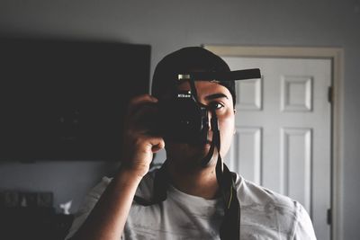 Portrait of young man holding camera at home