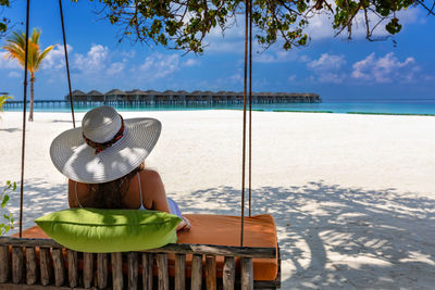 Rear view of woman relaxing on swing at beach during sunny day