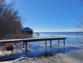 Scenic view of lake by building against clear blue sky during winter