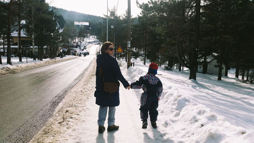 Rear view of mother and son walking on snow covered road