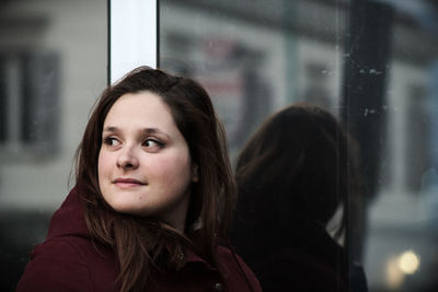 Close-up of beautiful woman looking away while standing glass wall