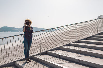 Full length of woman photographing with camera while standing on steps