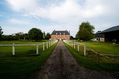 Street amidst field and houses against sky