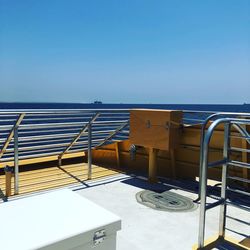 Chairs and table by sea against clear blue sky