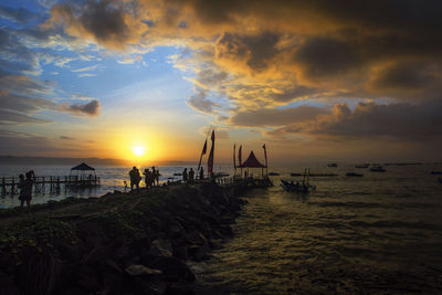 Silhouette people on beach against sky during sunset