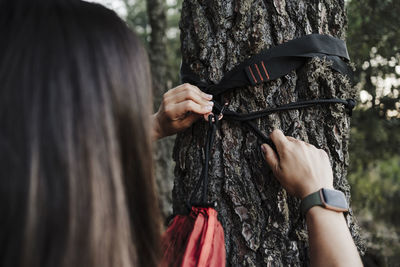 Young woman adjusting hammock to tree in forest during vacation