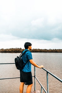 Rear view of man standing by railing against sky