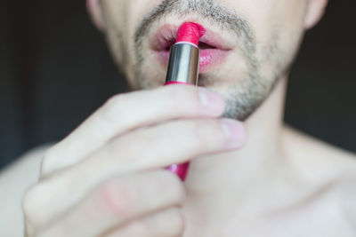Midsection of transgender man applying red lipstick