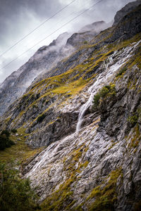 Scenic view of waterfall by mountains against sky