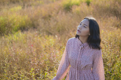 Young woman looking away while standing on field