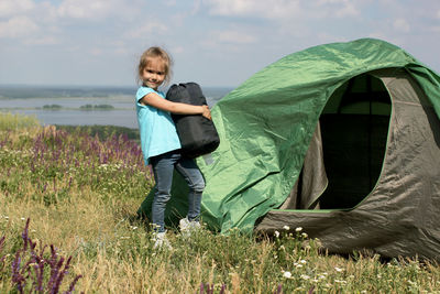 Cute 5 years old girl helping to pitch a tent on the campsite near beautiful landscape