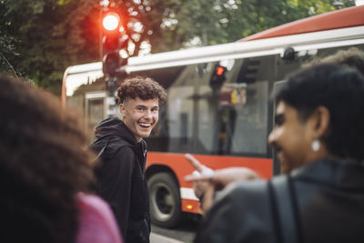 Side view of happy teenage boy looking at friends having fun at street