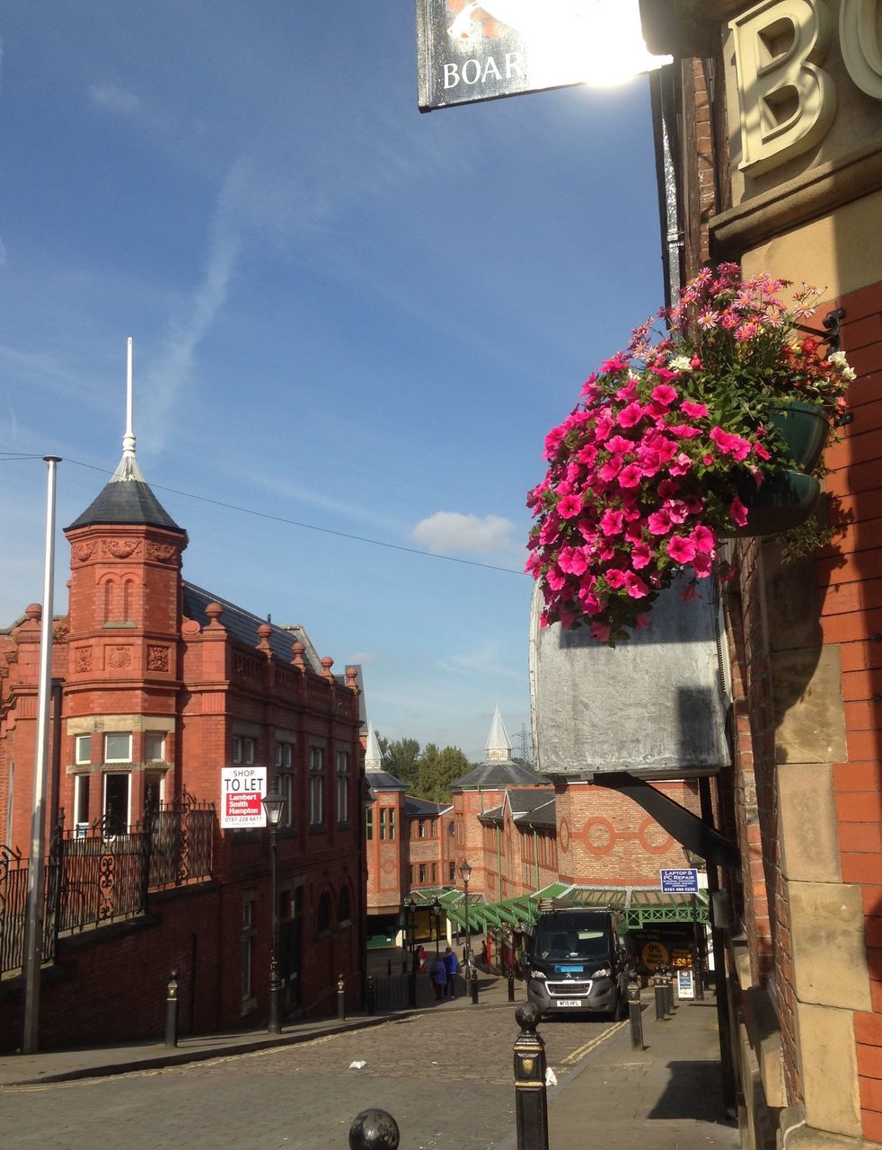 building exterior, architecture, built structure, car, street, road, city, land vehicle, transportation, flower, sky, incidental people, mode of transport, city life, tree, street light, day, sunlight, city street, outdoors